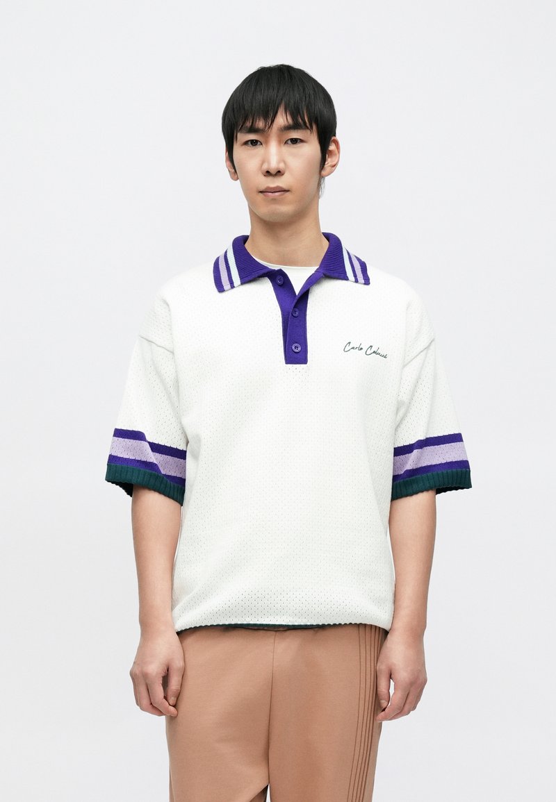 Biała koszulka polo o fakturowanym wyglądzie, z fioletowo-zielonymi paskami na rękawach i kontrastującym kołnierzykiem. Haft z napisem "Carlo C.".