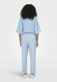 Top azzurro chiaro, morbido e fluido con maniche larghe abbinato a pantaloni tapered coordinati. Tessuto testurizzato e traspirante, con due tasche posteriori.