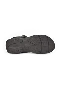 Suela de zapato deportivo negro con profundas ranuras para tracción, que presenta una superficie de goma lisa y un logo de la marca en relieve en la entresuela.