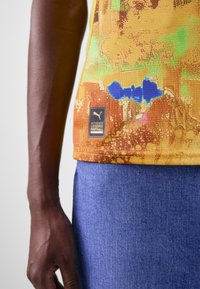 Maglietta da calcio Puma con un vivace motivo giallo e arancione con accenti blu, tessuto testurizzato e un'etichetta con il logo sull'orlo.