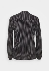 Schwarze Bluse mit langen Ärmeln und weißen geometrischen Mustern, mit Knopfverschluss hinten und gerafften Details an den Schultern. Leichter Stoff.