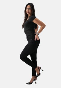 Czarne dopasowane dżinsy i czarna bluzka z krótkim rękawem połączone z czarnymi szpilkami. Szpilki mają kokardki i cienką szpilkową konstrukcję.