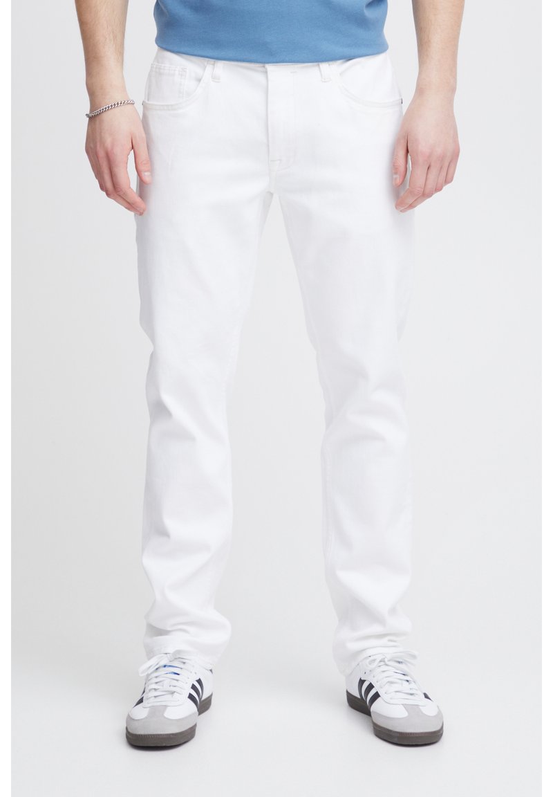 Vaqueros de mezclilla blancos con corte recto, cinco bolsillos y un ligero estiramiento, combinados con zapatillas gris y negras y una camiseta azul.