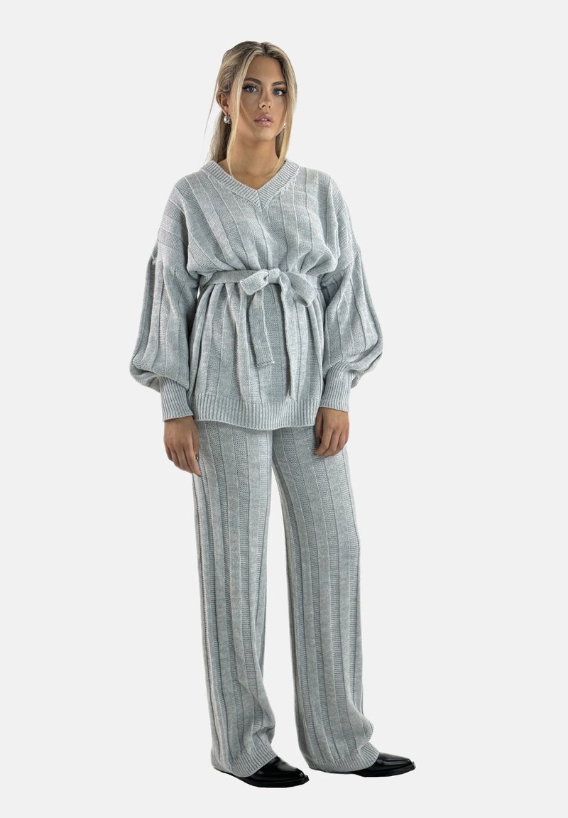 Completo grigio in maglia composto da un maglione e pantaloni con strisce verticali, maniche a palloncino, cintura da annodare e texture morbida, abbinato a calzature nere.