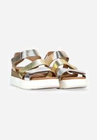 Correas metálicas en dorado, plateado y texturizadas con una plantilla beige, sobre una suela gruesa blanca, con un diseño casual de tipo slip-on.