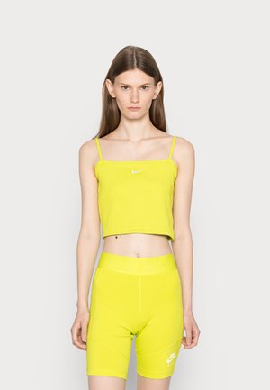 Een cropped, geribbelde tanktop en high-waisted fietsbroek in fel neongeel, met een klein wit logo op de borst en de broek.