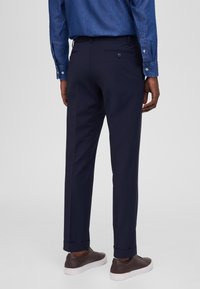 Pantalones de corte recto en color azul marino, confeccionados en una tela suave, con dos bolsillos traseros y puños doblados, combinados con zapatillas marrones.