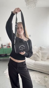 Jeune femme en tenue noire tenant un petit sac à bandoulière noir Karl Lagerfeld dans un salon lumineux et moderne.