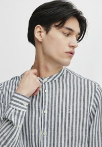 Camisa de manga larga, con botones, que presenta delgadas rayas verticales azules y blancas, un cuello mao y un sutil logotipo bordado. Tejido texturizado.