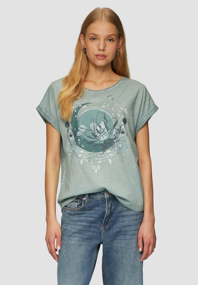 T-shirt bleu clair, ample, à manches courtes et à col rond. Présente un imprimé graphique floral dans des teintes plus foncées. Texture douce.