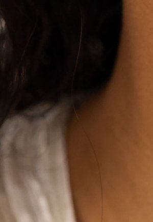 Cheveux noirs bouclés, tissu blanc et peau brun clair dans une composition en gros plan, avec un flou artistique et un éclairage chaud.