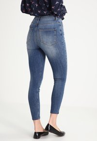 Jeans ajustados en denim azul medio con un acabado desgastado, que presentan una cintura alta, dos bolsillos traseros y un ajuste ceñido a lo largo de las piernas.