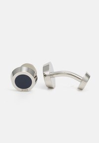 Cufflinks de ton argintiu cu un centru circular de nuanță navy și finisaj polisat. Dispune de un sistem de prindere curbat pentru fixare sigură. Logo embosat pe o parte.
