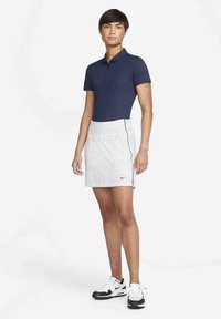 Modrá polo košeľa s krátkymi rukávmi, skombinovaná s bielou sukňou s čiernymi bodkami a bočnými akcentmi. Nosí sa s čierno-bielymi športovými topánkami.