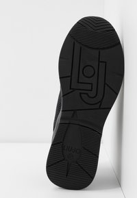 Black sneaker sole with textured rubber, featuring a logo and zigzag tread pattern. Smooth edges and structured design enhance grip.