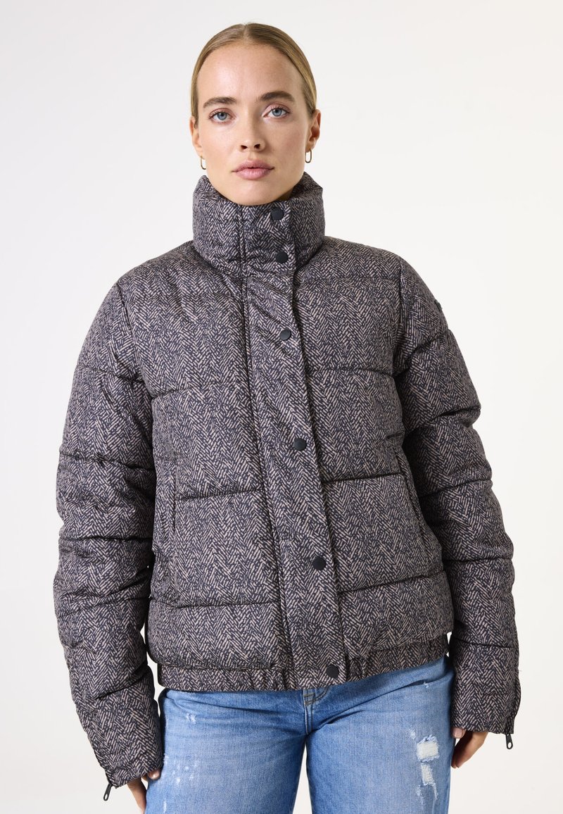 Veste rembourrée avec un col montant en motif chevrons, couleurs gris et marine, dotée de boutons pressions et de poignets élastiques.