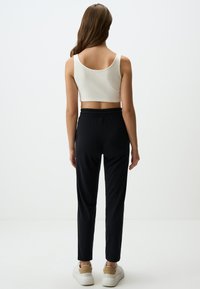 Weißes geripptes Crop-Top, schwarze Hose mit elastischem Bund und weiße Turnschuhe. Glatte Textur mit taillierter Passform und lässigem Schnitt.