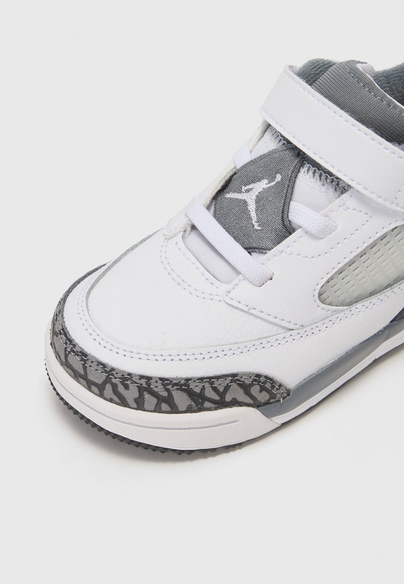 Witte sportieve schoen met grijze accenten, met een gestructureerde leren en mesh bovenkant, verstelbare band en een gestippelde grijze buitenzool.