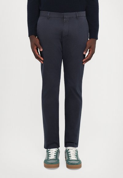 Marineblauwe katoenen broeken met een slim fit, voorzien van een knoop- en ritssluiting, voorkantzakken en subtiele stiksels, gecombineerd met groene sneakers.