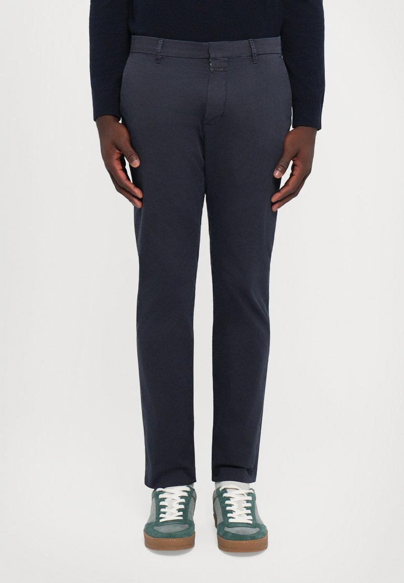Pantalon en coton navy avec une coupe slim, dotés d'une fermeture à bouton et à zipper, de poches avant et de détails de couture subtils, associés à des baskets vertes.