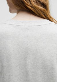 Grå sweatshirt med bred udskæring og tekstureret stof. Sømdetaljen løber lodret ned ad ryggen og fremhæver et afslappet design.