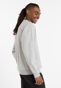 Grå, långärmad sweatshirt med ribbade muddar, avslappnad passform, sidovy visar en rundad halsringning och mjuk textur, bärs över svarta byxor.