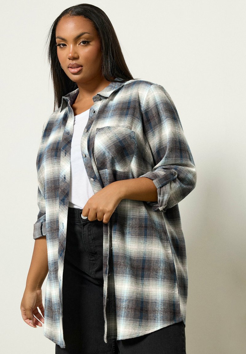 Långärmad rutiga skjorta med ett mönster i blått, svart och vitt, knappstängning framtill, och två bröstfickor, i kombination med svarta byxor.