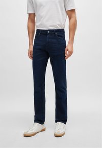 Blugi din denim albastru închis cu croi slim, având un fermoar, cinci buzunare și cusături subtile. Asortați cu adidași albi.