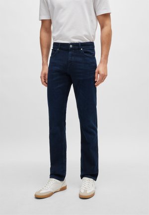 Donkerblauwe denim jeans met een slim fit, uitgerust met een ritssluiting, vijf zakken en subtiele stiksels. Gecombineerd met witte sneakers.