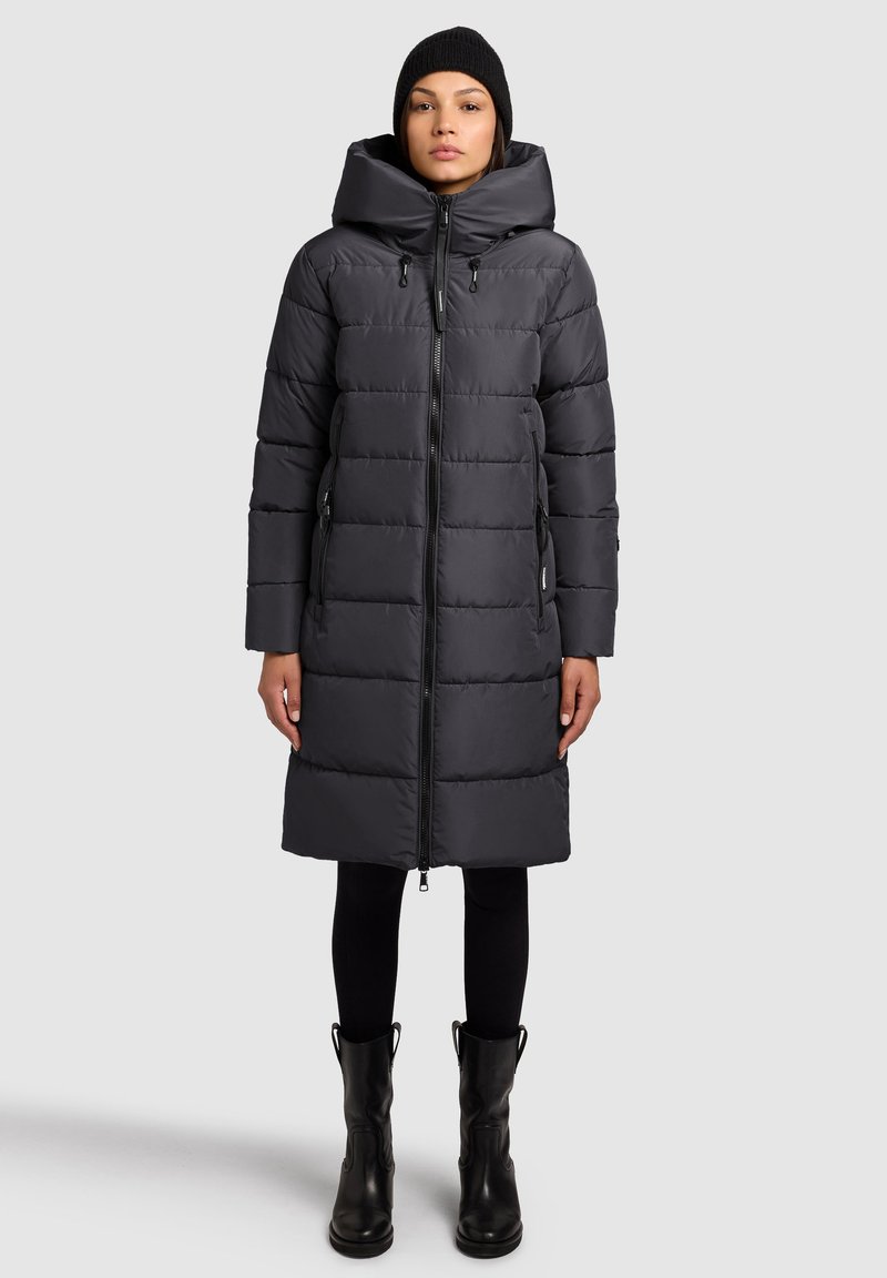 Čierny prešívaný kabát s vysokým golierom a veľkou kapucňou. Má predný zips, dve bočné vrecká a stredne dlh�ý strih. Hladká textúra.