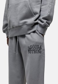 Grijze sweatshirt met kangoeroezak, geribde manchetten en bijpassende grijze joggingbroek met een bedrukte "GOOD FOR NOTHING" logo op de dij.