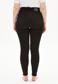 Jeans ajustados negros de talle alto, confeccionados en denim, con dos bolsillos traseros y un diseño limpio y sin costuras. Textura suave y silueta ajustada.