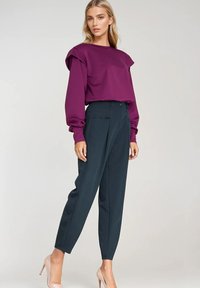 Fioletowa bluzka z długim rękawem i bufkami, zestawiona z ciemnymi spodniami z wysokim stanem oraz cielistymi szpilkami. Gładkie faktury w całym zestawie.