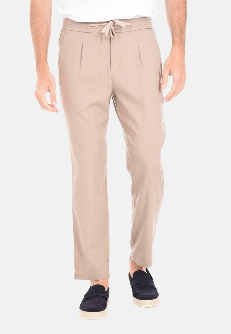 Pantaloni beige su misura con vita con cordoncino, frontale plissè e gambe affusolate. Il tessuto è liscio con una texture leggera.