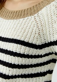 Pull en maille avec un col côtelé beige, des rayures alternées noires et blanches, et une texture lâche, mettant en avant un design décontracté.