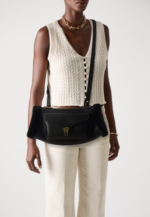 Black leather handbag with a textured finish, featuring plush black side accents and a gold clasp. Worn casually with a beige knit top and light pants.