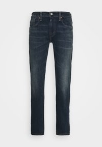 Jean slim bleu foncé avec poches avant, passants de ceinture, fermeture à boutons et détails légèrement délavés sur les cuisses et les genoux.