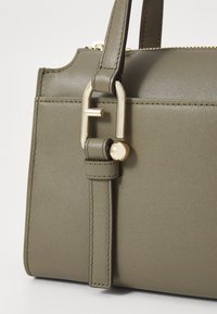 Sac à main en cuir vert olive avec un design structuré, doté d'un accent en métal doré et d'une sangle détaillée pour une fermeture sécurisée.