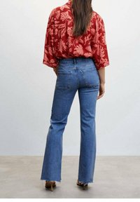 Blusa a fiori rossi con maniche ampie abbinata a jeans blu a zampa d'elefante con orlo sfrangiato. Modello visibile di spalle.