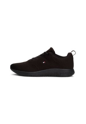 Black low-top sneaker with textured knit upper, black sole, pull tab on heel, and small red, white, and blue logo on side.