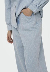 Lichtblauwe denimtop met een geometrisch patroon, voorzien van een bandkraag en knoopmanchetten, gecombineerd met bijpassende losse broek.