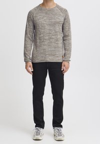 Pull gris chiné avec des manches longues et un col rond, associé à un pantalon noir et des baskets gris clair. Le pull présente un ourlet et des poignets côtelés.