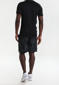 Mustat lyhythihaiset paidat yhdistettyinä mustiin kuosisortseihin, joissa on geometrisia kuvioita, ja harmaisiin urheilukengiin.