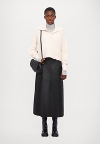 Ljusrosa kort tröja med bred krage, lagd över en grå polotröja. Svart fusk läder midi-kjol och svarta ankelboots fulländar outfiten.