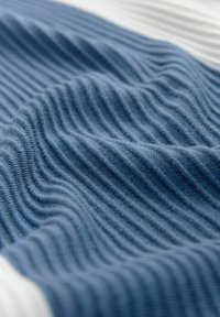 Knitted fabric in dark blue with fine, vertical ribbed texture, showcasing soft, flexible drape. White accents visible in the background.