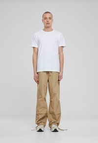 Witte katoenen t-shirt gecombineerd met beige losse broek. De broek heeft een trekkoord in de taille en geplooide details aan de onderkant.