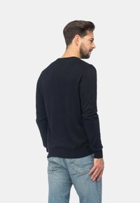 Maglione nero a collo rotondo realizzato in tessuto morbido, con maniche lunghe, polsini e orlo a costine. Indossato sopra jeans in denim blu, mostra un design semplice.