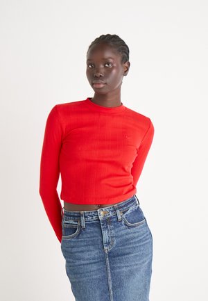 Röd ribbad långärmad crop top med rund halsringning, parat med en högmidjad blå denimkjol som har en lätt blekning och klassiska fickor.