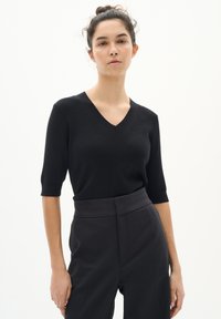 Top tricotat negru cu decolteu în V și mâneci scurte, asociat cu pantaloni negri cu talie înaltă. Textură netedă și design ajustat.