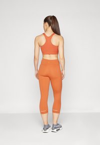 Oranžový športový crop top a legíny, priliehavý strih, elastický materiál, s reflexnými detailmi na manžetách členkov, v kombinácii so sivými teniskami.